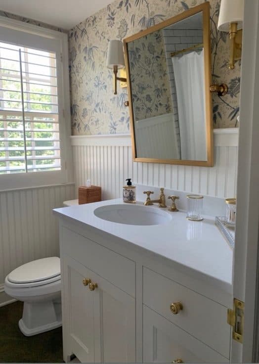 Bathroom vanity with botanical wallcovering, brass sconces, and a pale double sink.