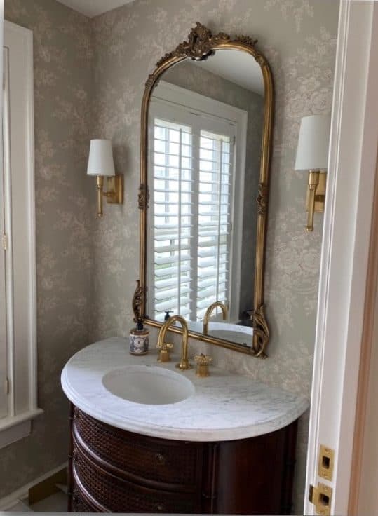 Bathroom mirror and brass sconce detail with patterned wallcovering.