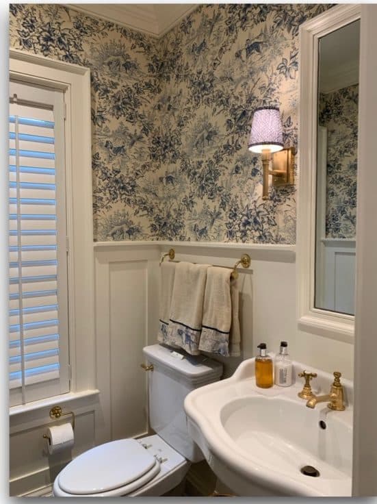 Bathroom sink nook with floral wallcovering, brass fixtures, and wainscoting.