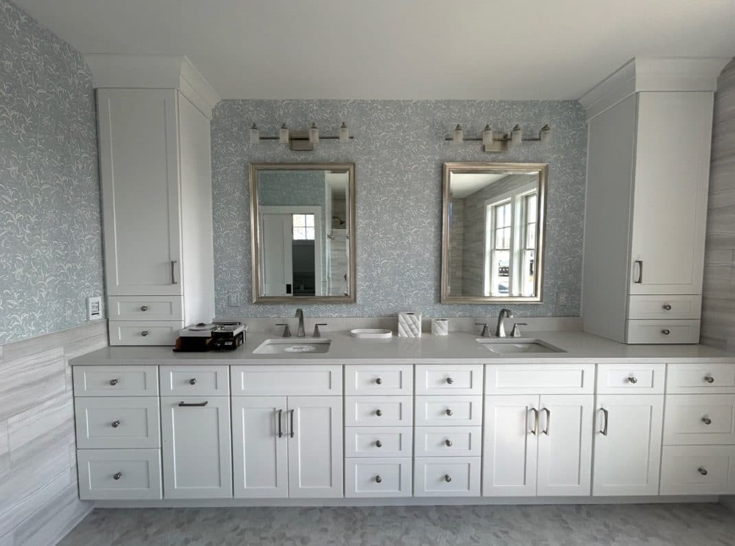 Bathroom double vanity with pale cabinetry, framed mirror, and patterned valance.