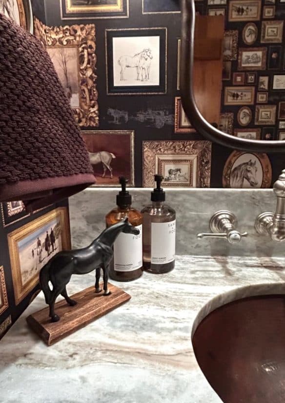 Powder room vanity with dark patterned wallcovering, marble counter, and curved mirror.
