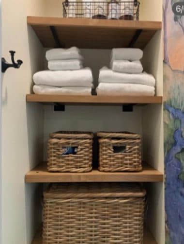 Bathroom towel shelving with baskets, hooks, and colorful wallcovering nearby.