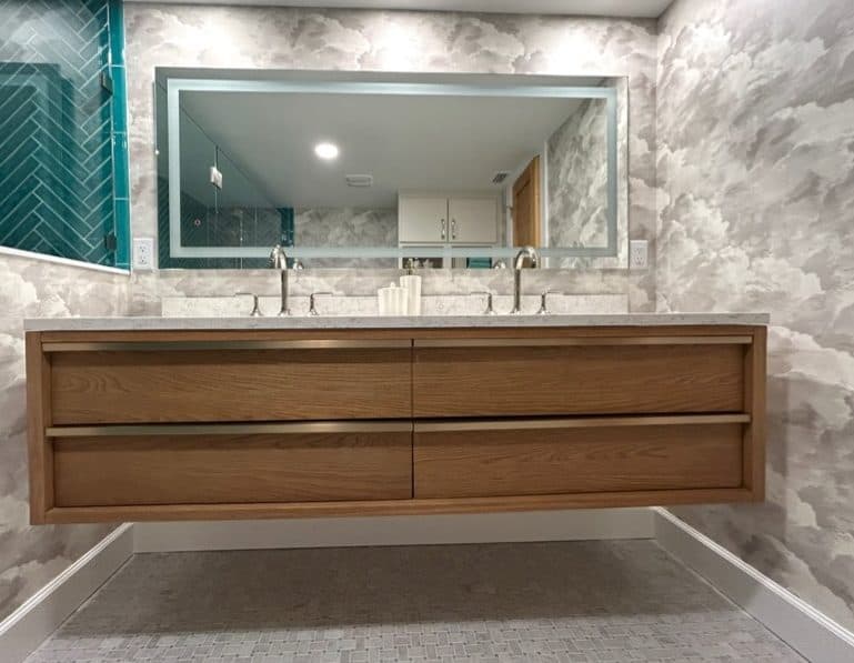 Bathroom vanity with wood drawers, stone counter, large mirror, and gray wallcovering.