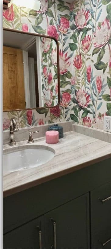 Bathroom vanity with floral wallcovering, green cabinetry, and bright pink towels.