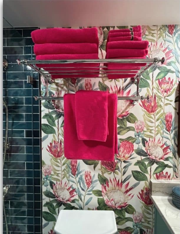 Bathroom towel storage with teal tile and floral wallcovering.
